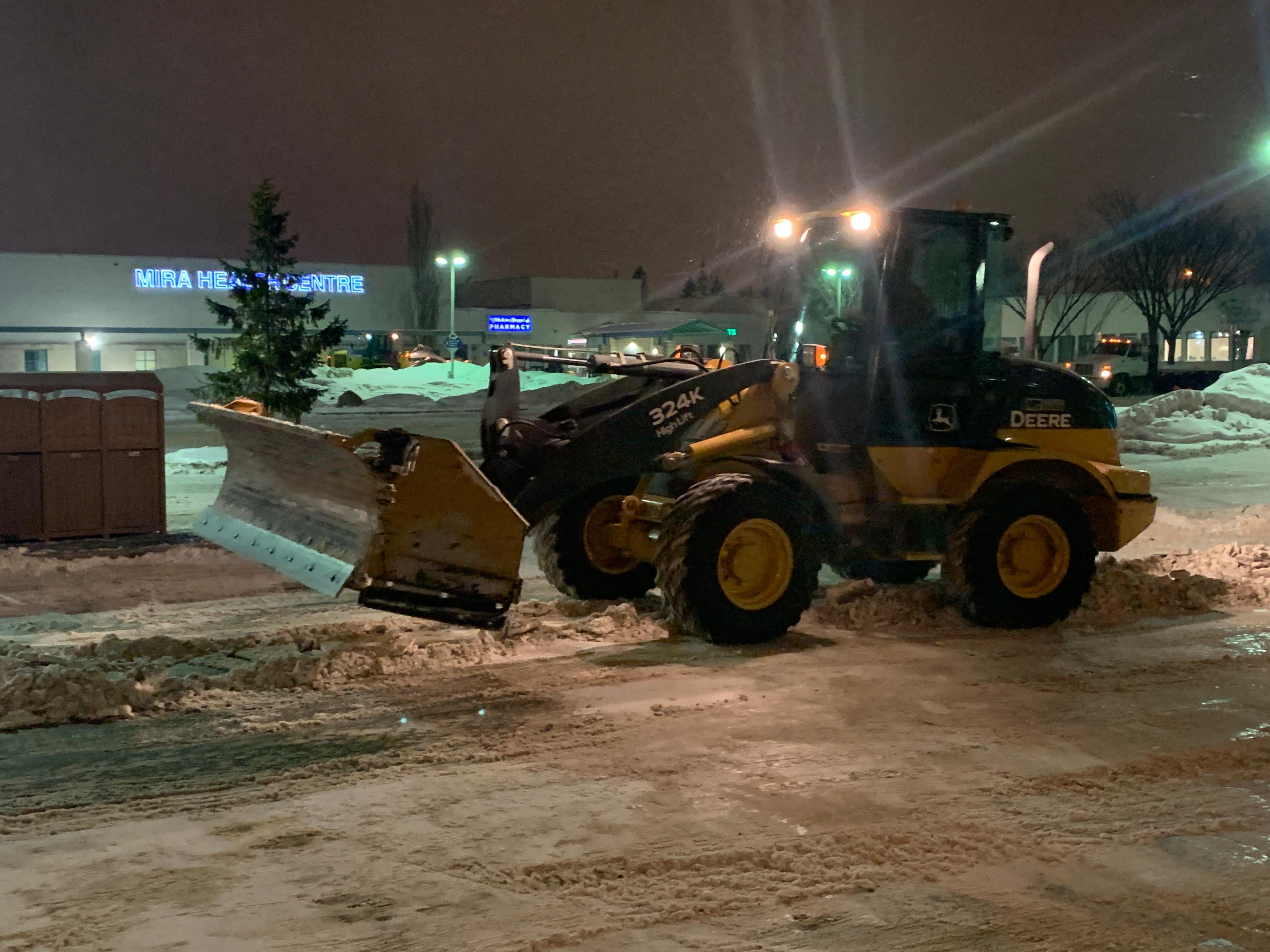 John Deere wheel loader plowing snow at night beside commercial health centre